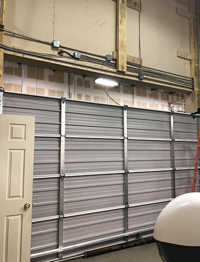 A modern garage door with a sleek design, featuring horizontal panels in a dark color, set against a light-colored house exterior.