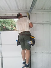 A modern garage door with a sleek design, featuring horizontal panels and a light gray color, set against a brick wall and a green lawn.