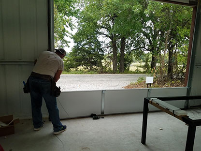 A modern garage door with a sleek, horizontal design in a light gray color, set against a brick wall. The door features large glass panels that allow natural light to enter the garage, enhancing the contemporary aesthetic.